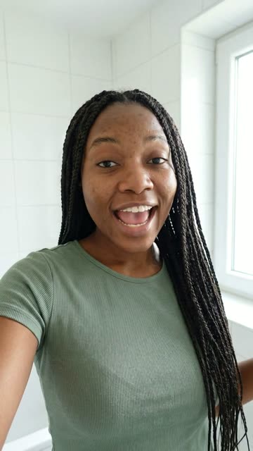 A vertical ad: a woman with long braids in a bright white bathroom, talking to the camera.